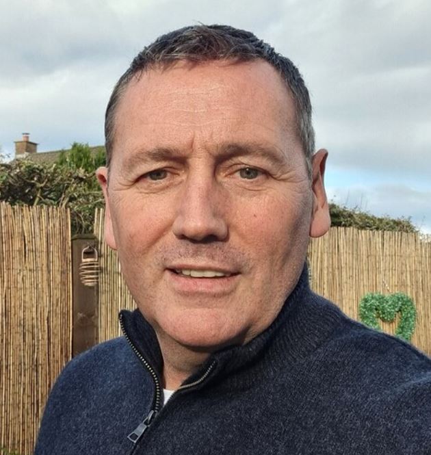 Picture of a man standing in an outside setting with a fence in the background