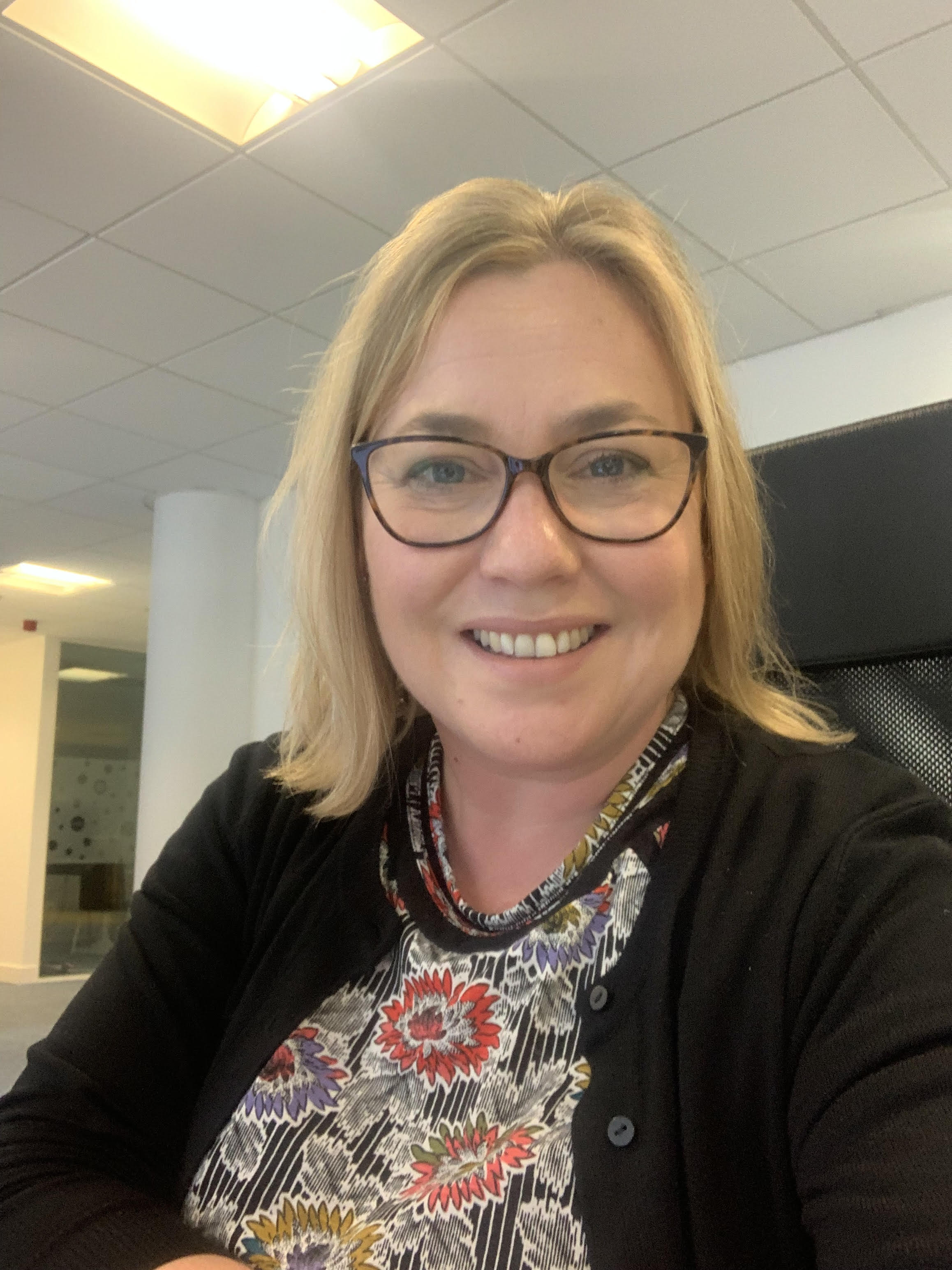 Lady wearing glasses wearing a pattered top and a black cardigan