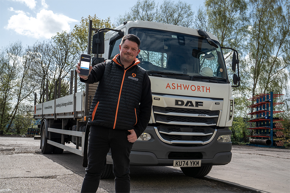 Man in a black jacket standing in front of a truck holding a mobile phone.