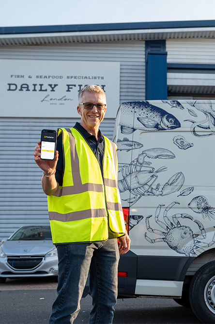 Smiling man holding a mobile device standing in front of a Daily Fish Supplies depot