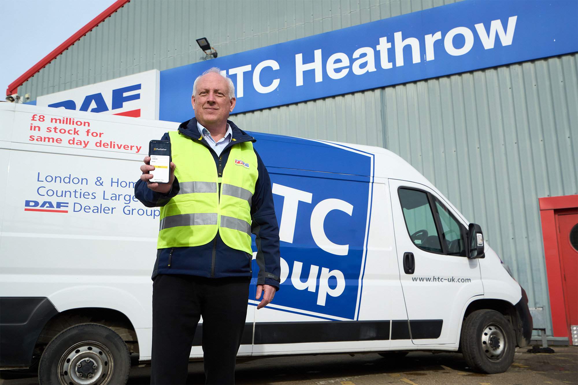 Man in a high vis vest standing in front of a van holding a mobile device