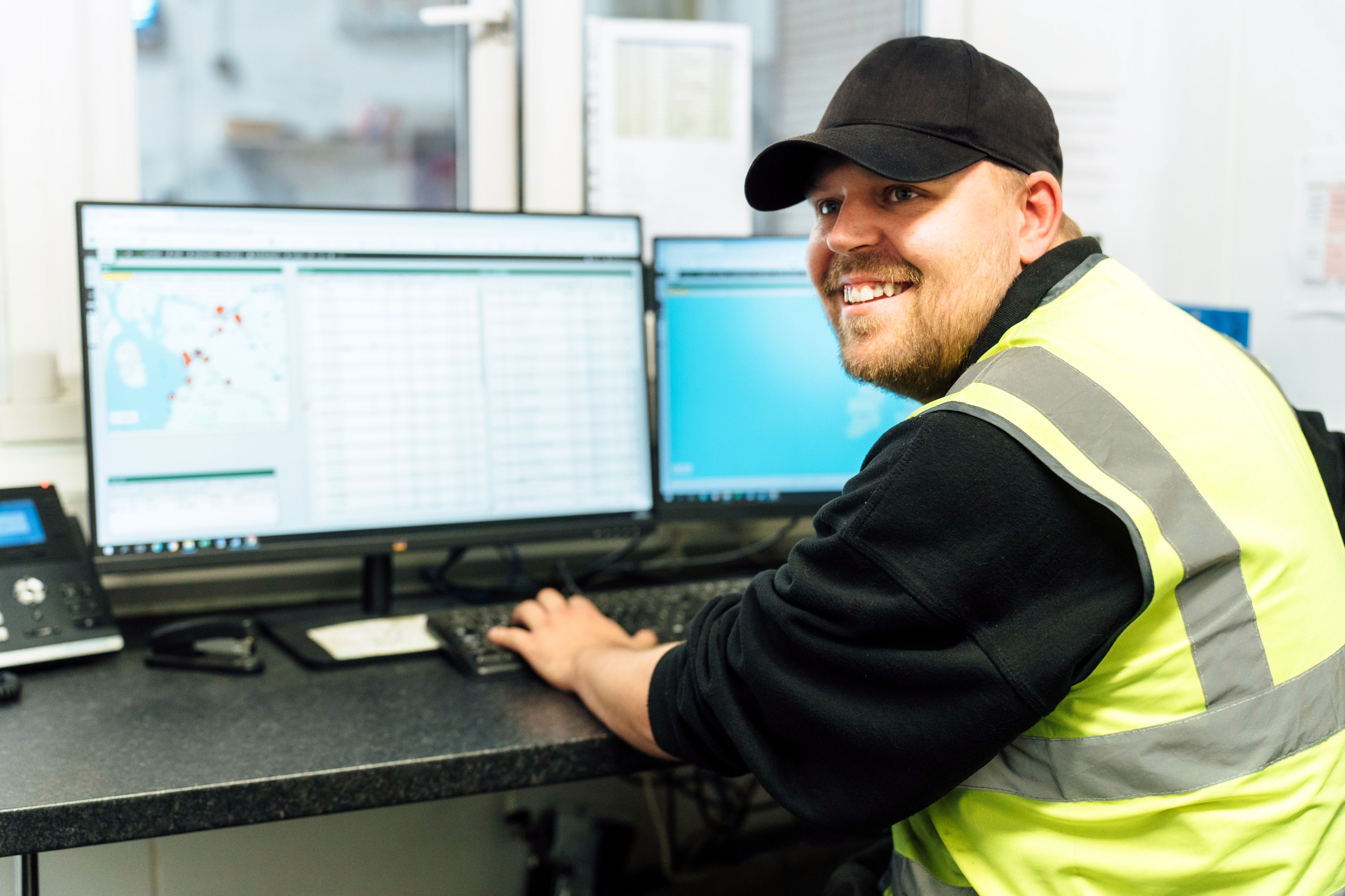 Man wearing a cap and high vis vest sitting in front of a computer